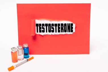 Beyaz arka planda kırmızı kağıt, şırınga ve hormon dolu kavanozlarda testosteron harfleri.