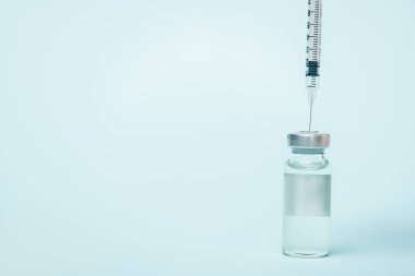 Syringe in jar of vaccine with hormone on blue surface with copy space clipart
