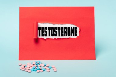 Mavi arka planda kırmızı kağıt deliğinde hormon hapları ve testosteron harfleri.
