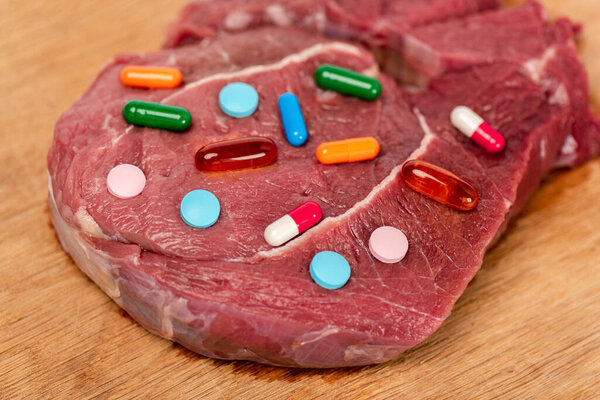 Вид гормональных таблеток на кусок сырого мяса на деревянной поверхности
