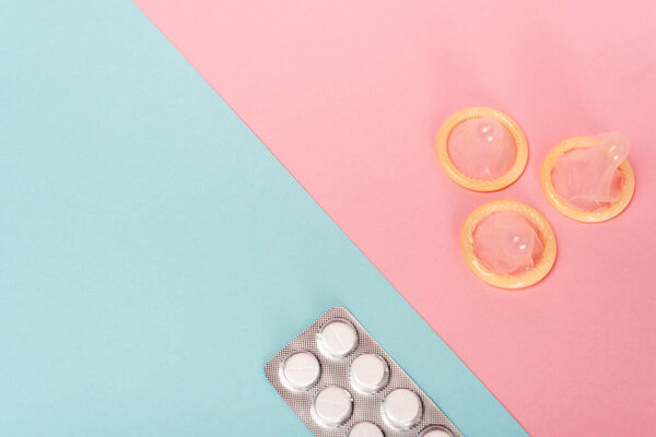 Вид сверху на волдырь с противозачаточными таблетками и кондомами на розовой и голубой поверхности
