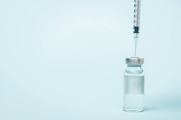 Syringe in jar of vaccine with hormone on blue surface with copy space