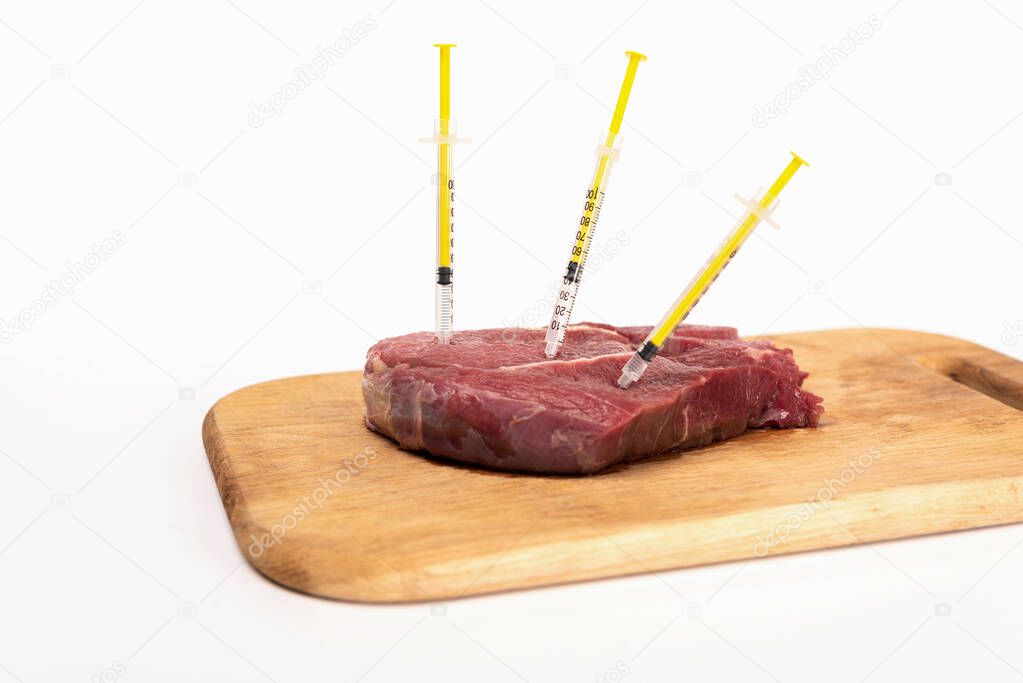 Syringes in raw meat on wooden chopping board isolated on white