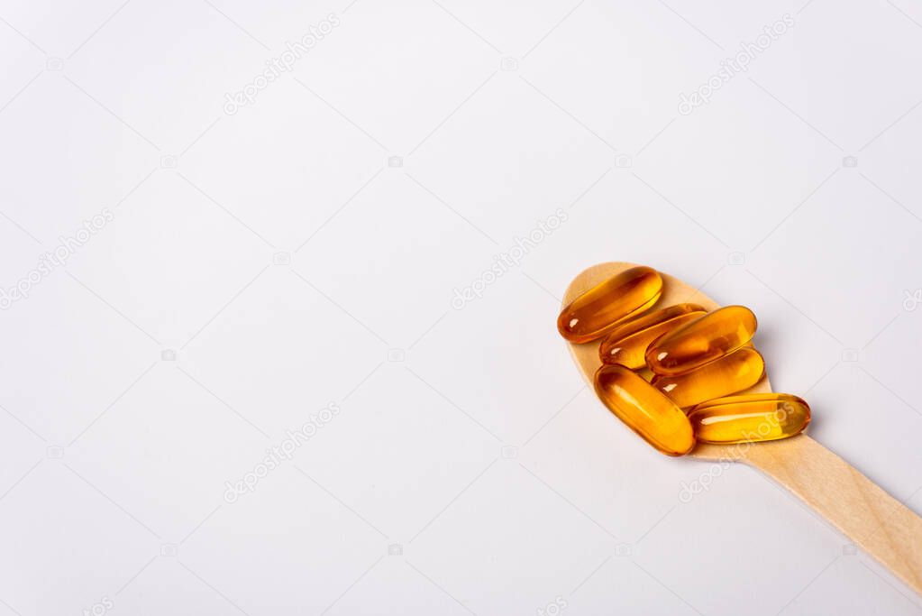 High angle view of wooden spoon with pills of omega 3 on white background
