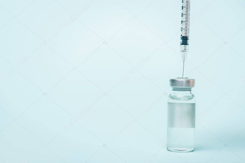 Syringe in jar of vaccine with hormone on blue surface with copy space