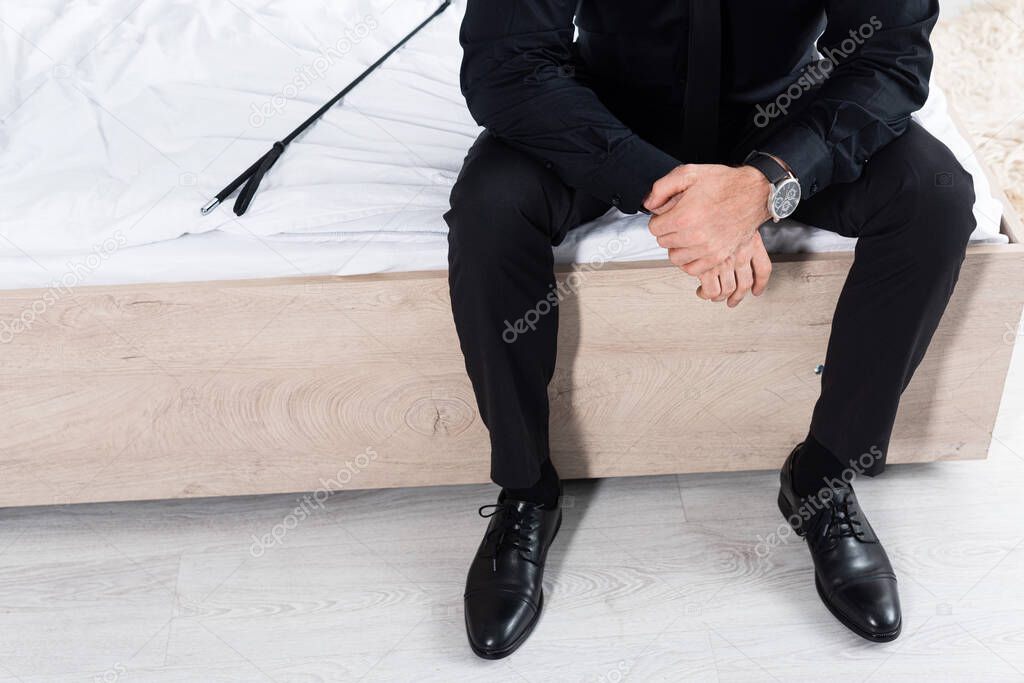 Cropped view of man near flogging whip sitting on bed
