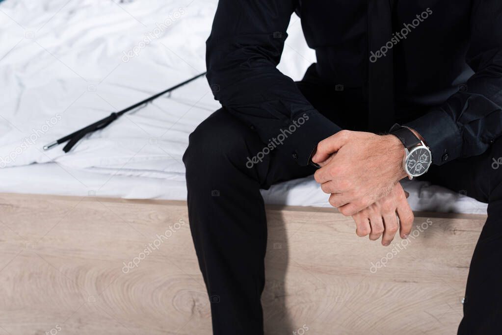 Partial view of man near flogging whip sitting on bed