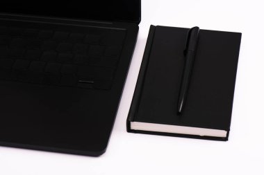 Siyah dizüstü bilgisayarın yanındaki defter ve kalem beyaza izole edilmiş. 