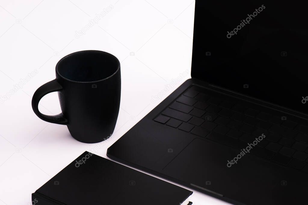 notebook and cup near black laptop on white 