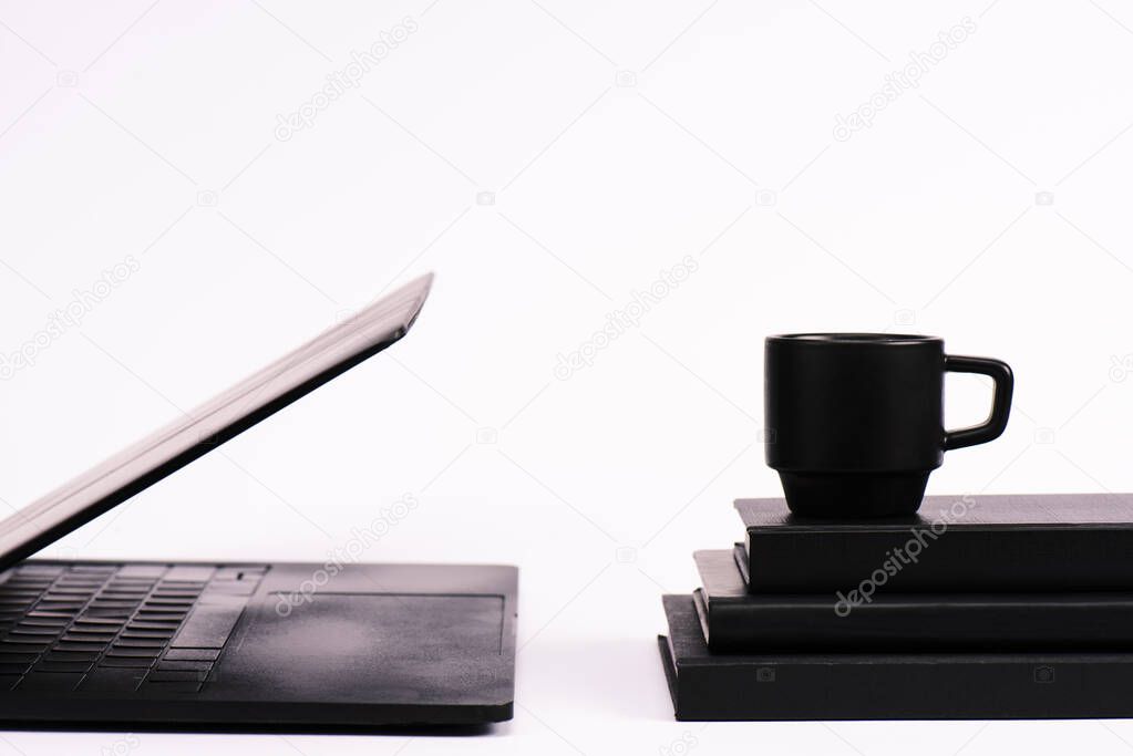 cup on notebooks near black laptop on white 