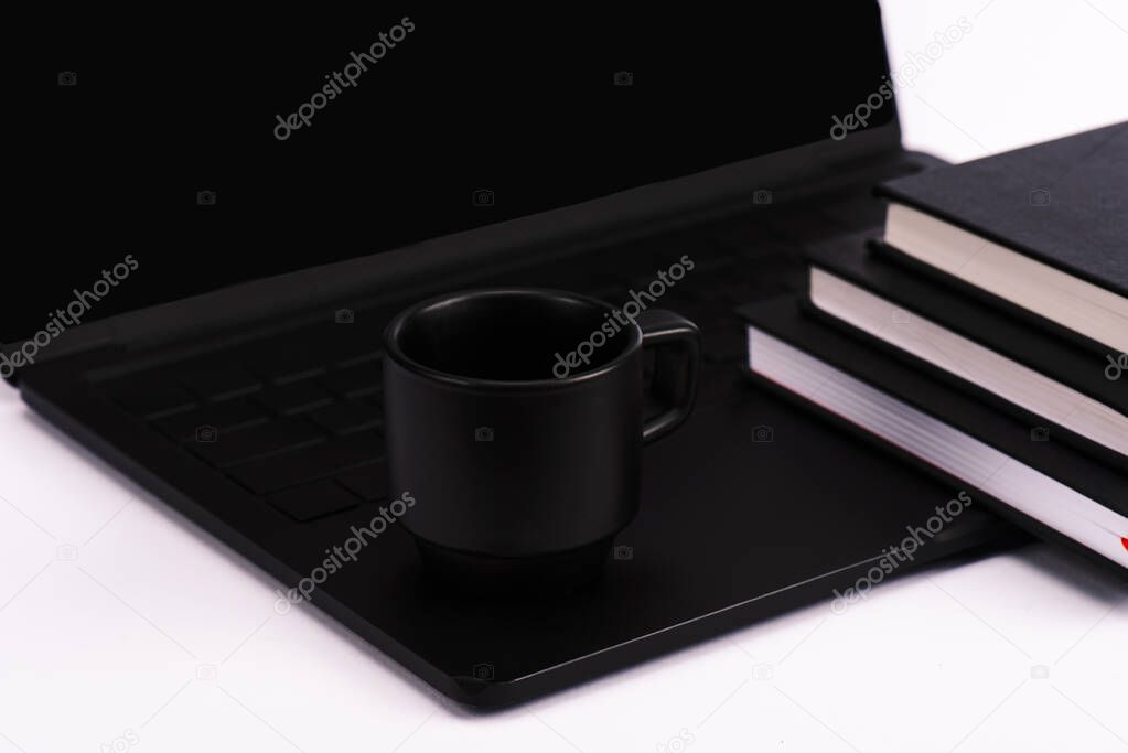 notebooks and cup near black and modern laptop isolated on white 