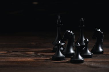 chess figures on wooden surface isolated on black  clipart