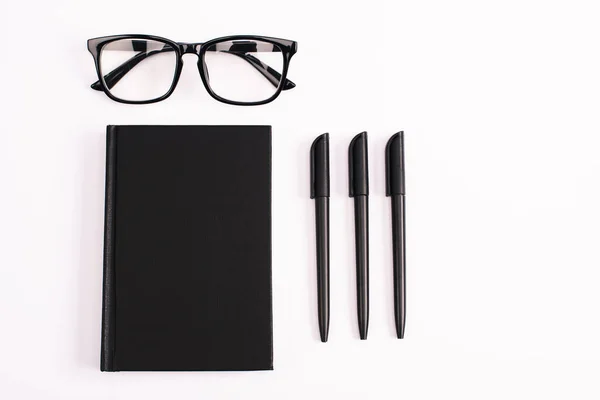 Tendido Plano Con Bolígrafos Cerca Gafas Cuaderno Negro Aislado Blanco — Foto de Stock