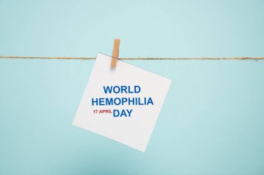 Card with world hemophilia day lettering on rope with pin isolated on blue clipart
