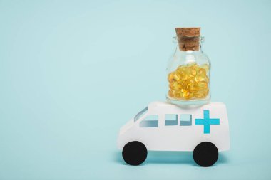 Mavi arka planda oyuncak ambulans arabasında bir kavanoz hap.