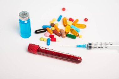 Kan örneğiyle test tüpü, haplar ve beyaz arka planda aşılı şırınga.