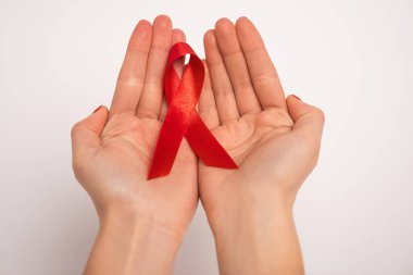 Cropped view of woman holding red ribbon of aids awareness on white background clipart