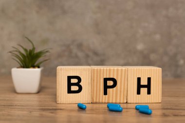 Selective focus of cubes with bph letters and pills with plant on wooden table on grey background clipart