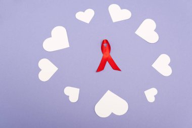 AİDS 'in kırmızı kurdelesinin yüksek açılı görüntüsü ve mor üzerine izole edilmiş kağıt kalpler.