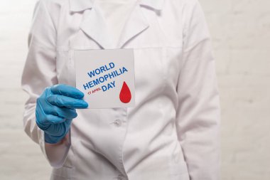 Cropped view of doctor holding card with world hemophilia day on white background clipart