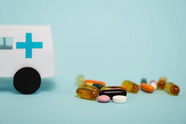 蓝色背景的药片和玩具救护车的选择性聚焦 — 图库照片