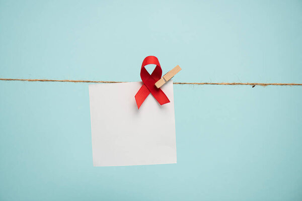 Empty card with aids awareness red ribbon on rope with pin isolated on blue 