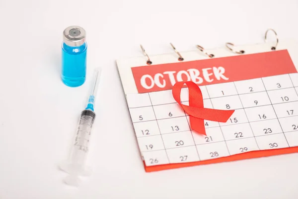 10月とカレンダーの選択的な焦点は 白い表面に注射器と認識赤いリボンを支援します — ストック写真