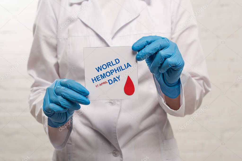 Cropped view of doctor in latex gloves holding card with world hemophilia day on white background