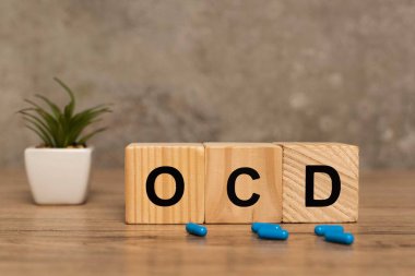 Selective focus of ocd letters on cubes near pills and plant on wooden surface on grey background clipart
