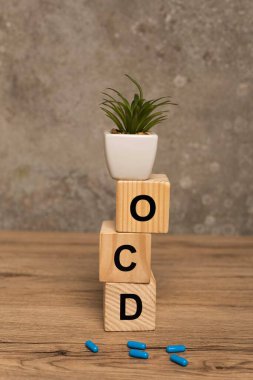 Plant on stacked cubes with ocd letters and pills on wooden surface on grey background clipart
