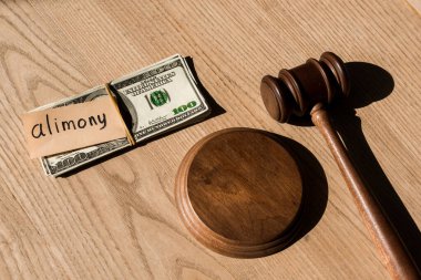 Dolar banknotlarının yanındaki tokmağın en üst görüntüsü ve tahtadan masasında nafaka yazıları olan kağıt.