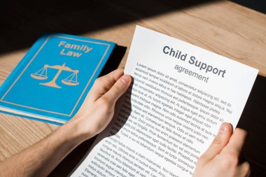 cropped view of man holding document with child support agreement near family law book on desk  clipart