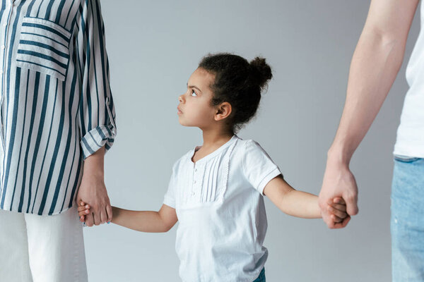 sad african american kid holding hands with divorced foster parents isolated on grey  