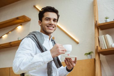 Low angle view of businessman with saucer and cup of coffee looking at camera and smiling  clipart