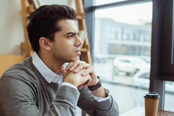 Thoughtful businessman with clenched hands near paper cup of coffee at table in office