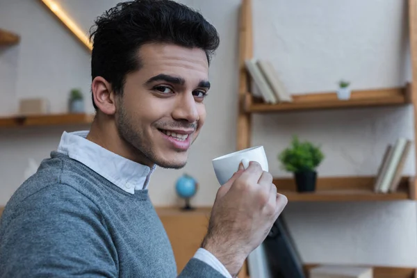 Biznesmen Uśmiechnięty Patrzący Kamerę Trzymający Filiżankę Kawy Biurze — Zdjęcie stockowe