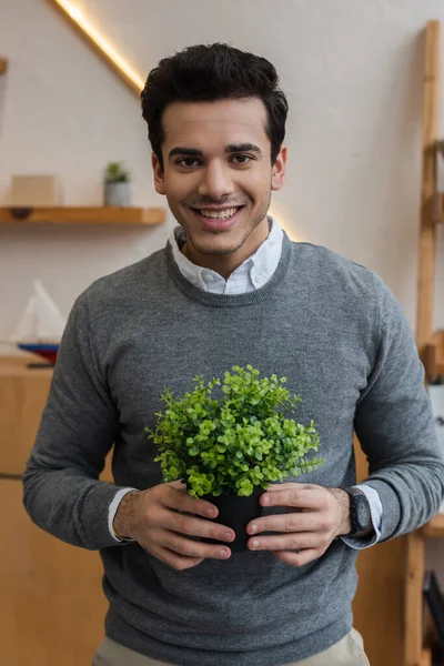 Çiçek saksısıyla gülümseyen ve kameraya bakan işadamlarının önünde.