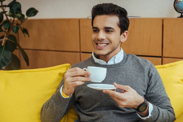 男人笑着 拿着茶托和咖啡在沙发上 — 图库照片