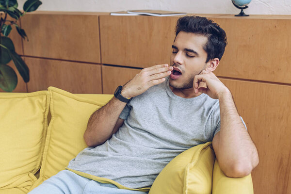 Man yawning and covering mouth on sofa in living room