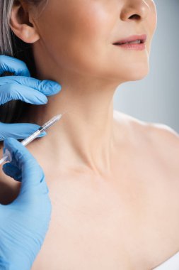 Plastik eldivenli, gülümseyen çıplak kadın ve doktor ellerinde gri üzerinde güzellik enjeksiyonu olan bir şırınga vardı.