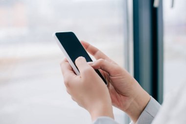 Ofisteki pencerenin yanında boş ekranlı akıllı telefon kullanan profesyonel iş kadını görüntüsü 