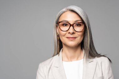 attractive smiling asian businesswoman in eyeglasses isolated on grey clipart