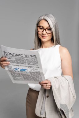 Gözlüklü gülümseyen Asyalı iş kadını Grey 'de izole edilmiş iş gazetesi okuyor.
