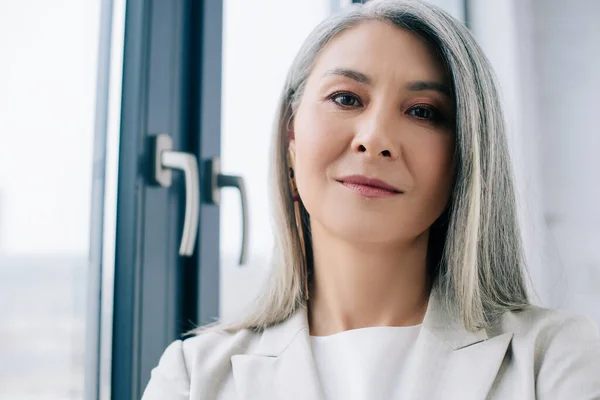 confident asian businesswoman with grey hair in grey suit in office