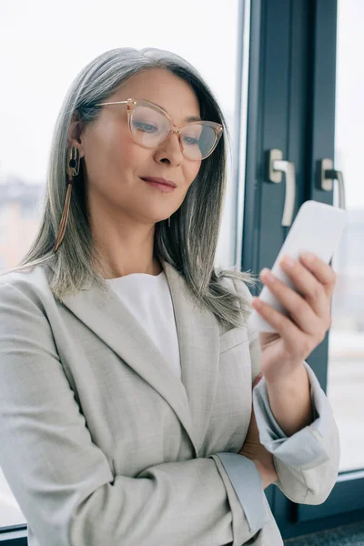 Atraente Asiático Empresária Óculos Com Cabelos Grisalhos Usando Smartphone Escritório — Fotografia de Stock