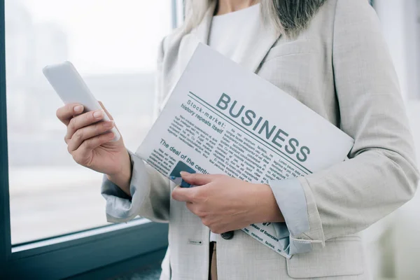Cropped View Businesswoman Using Smartphone Holding Business Newspaper Office — Stock Photo, Image