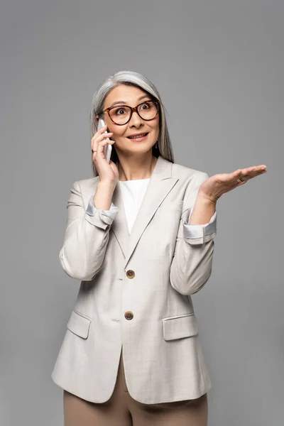 Surprised Asian Businesswoman Eyeglasses Grey Hair Talking Smartphone Isolated Grey — Stock Photo, Image