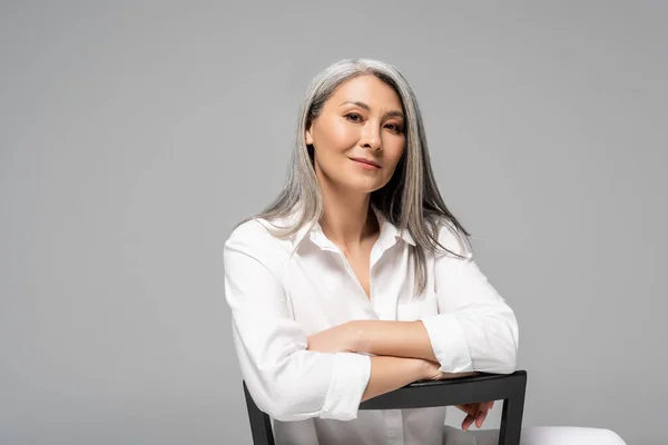 Aantrekkelijke Aziatische Vrouw Met Grijs Haar Zitten Stoel Geïsoleerd Grijs — Stockfoto