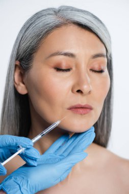 Güzel, çıplak Asyalı kadın ve doktor lateks eldivenli ellerinde gri üzerinde güzellik enjeksiyonu olan bir şırınga tutuyorlar.