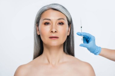 Güzel, çıplak Asyalı kadın ve doktor lateks eldivenli ellerinde gri üzerinde güzellik enjeksiyonu olan bir şırınga tutuyorlar.